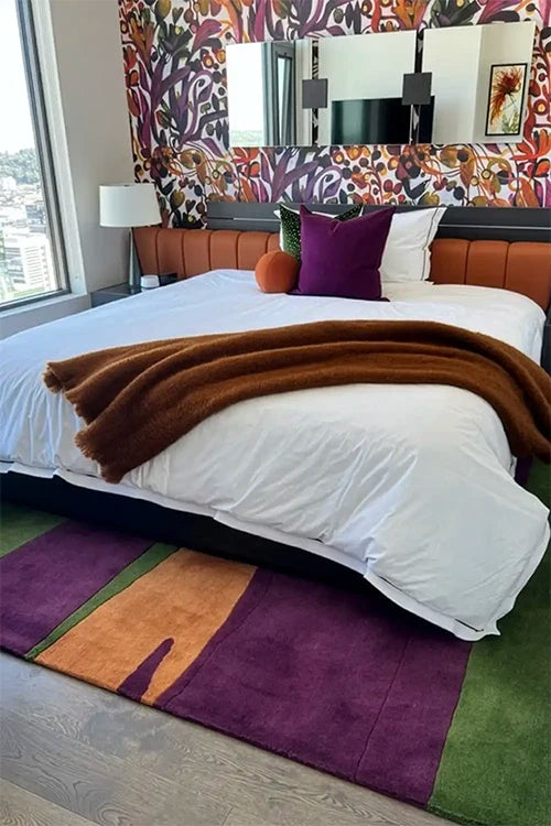 Bedroom with a bed featuring a brown blanket and colorful rug, next to a patterned wall and large mirror.
