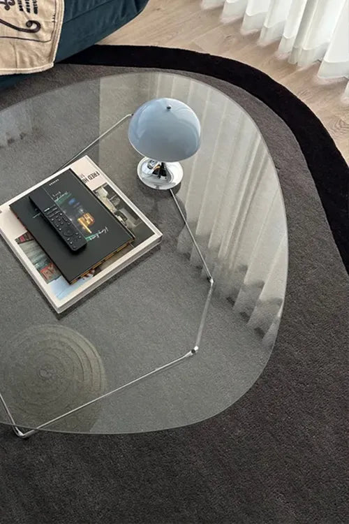 Glass coffee table with a smartphone, book, and small globe on a dark rug.