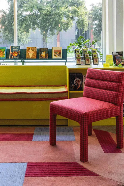 Colorful room with an oval rug,  yellow bench, red plaid chair, and books on a shelf.