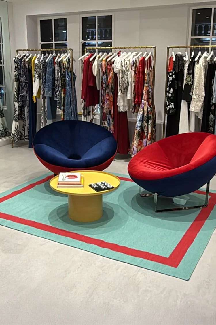 Modern interior with colorful chairs and a round table and woven rug in a room with clothing racks.