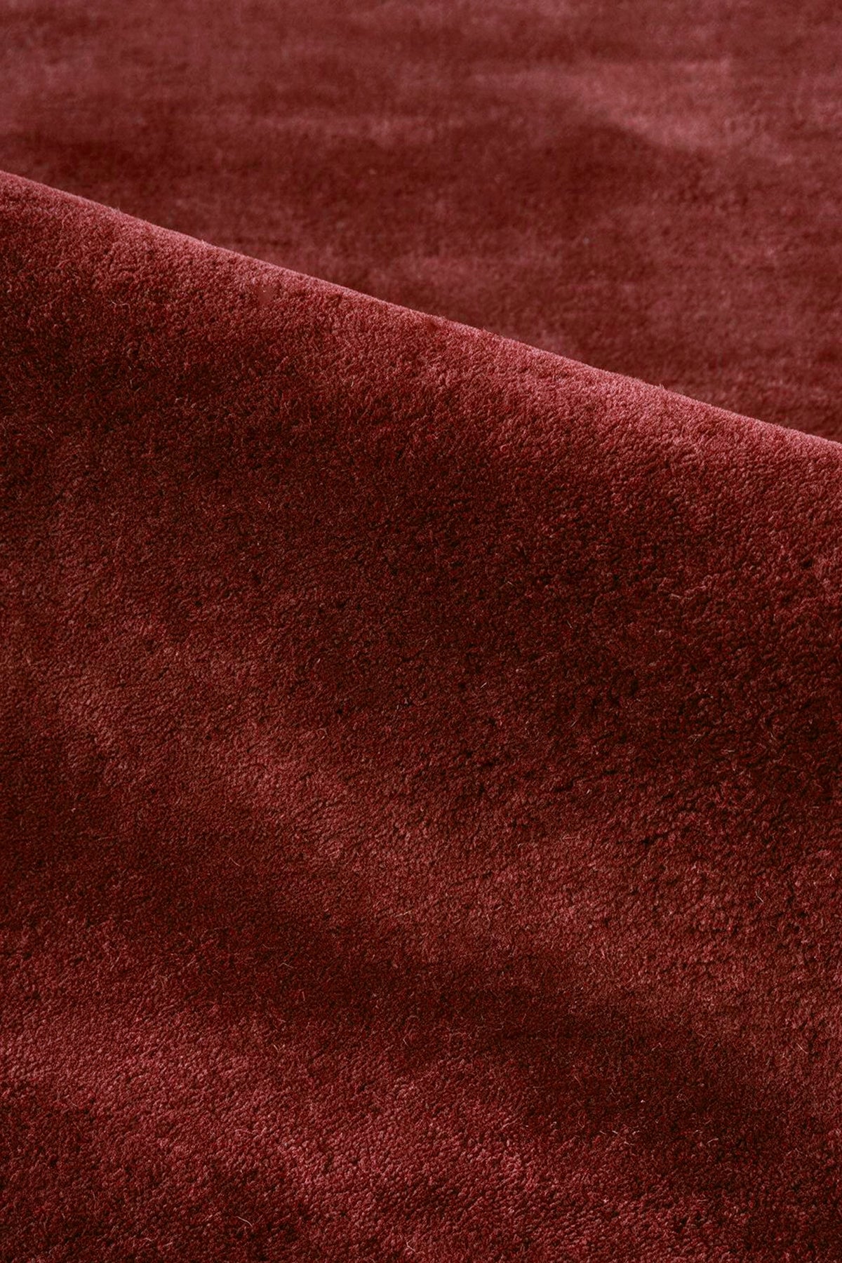A close-up of a plush, deep burgundy rust wool rug with soft folds and a rich texture.