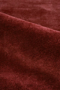 A close-up of a plush, deep burgundy rust wool rug with soft folds and a rich texture.