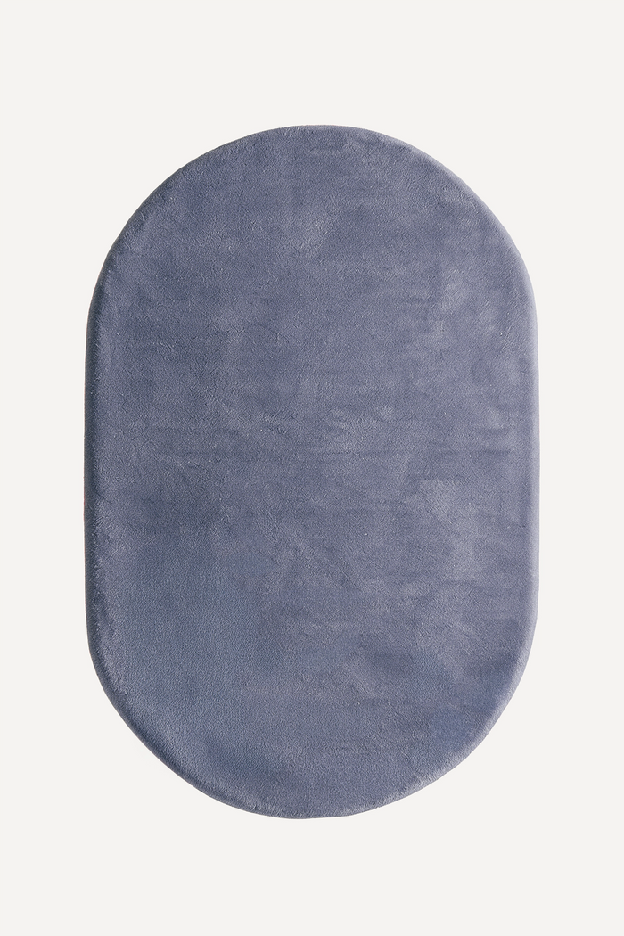 An oval-shaped plush rug in a slate dusty blue color, shown from a top-down view on a clean off-white background.