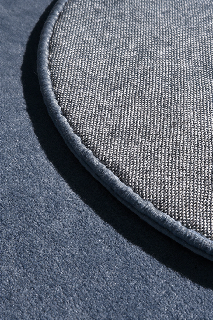 close up detail of a dusty blue rug lifted to show edge binding and cotton backing | Cotton backing