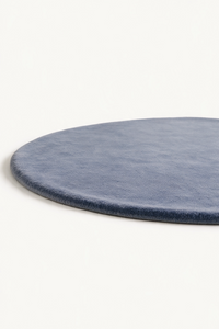 A close-up of a round dusty blue wool rug shown on a plain off-white background.