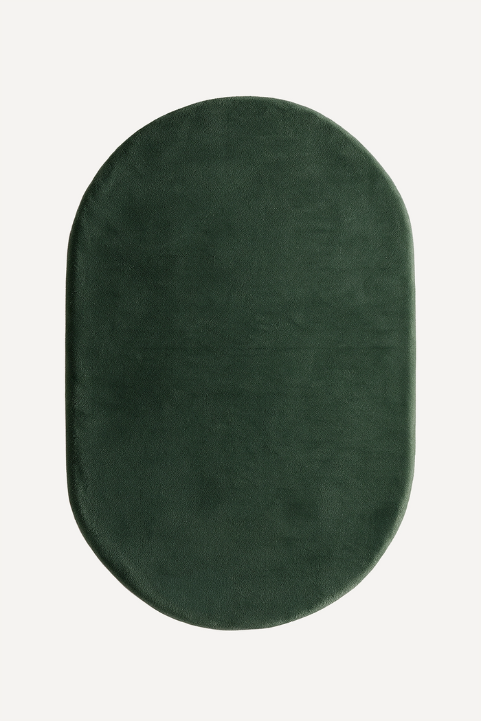 A dark forest green oval rug with rounded corners, shown from a top-down view on a light off-white background.