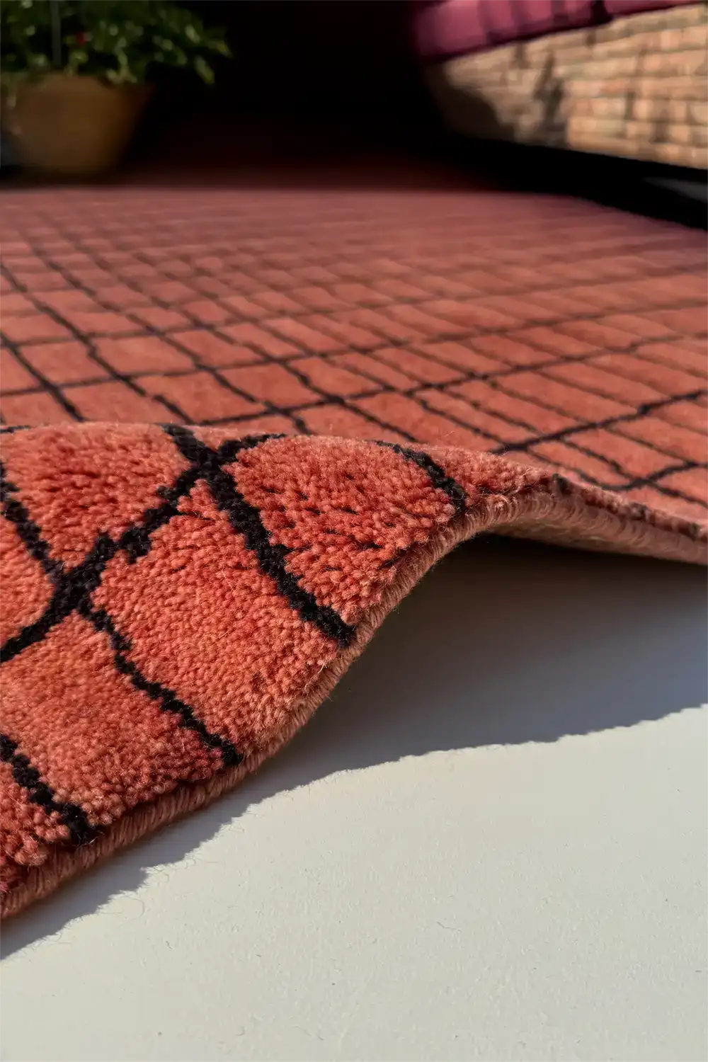 Close-up of a rust red rug with black grid pattern on a light surface in a bedroom lifestyle