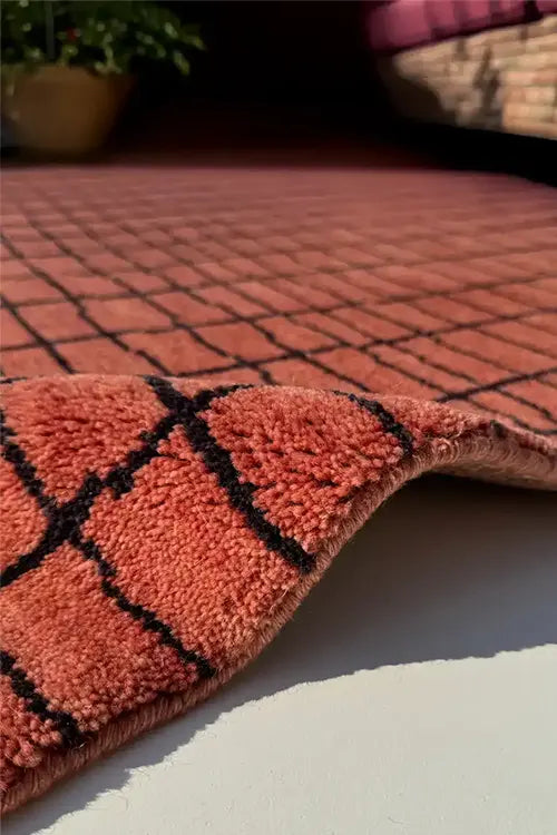 Close-up of a textured orange rug with black lines on a light surface.