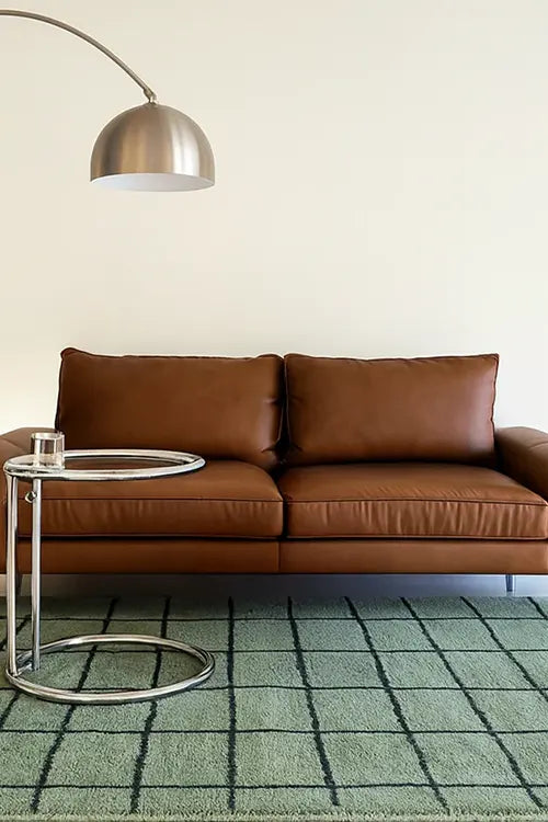 Brown leather sofa in a living room with a green checkered rug and a floor lamp.