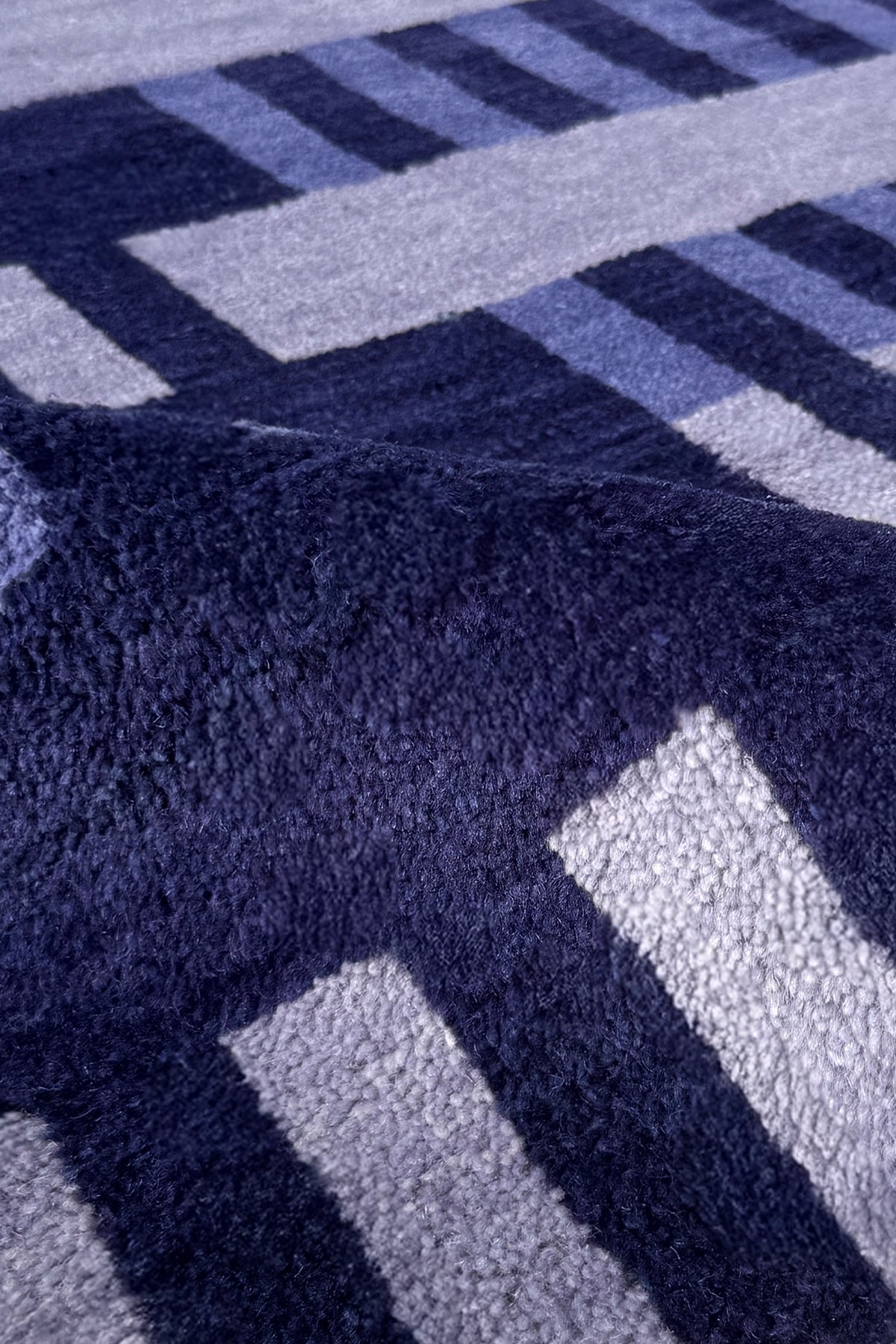 Close-up of a plush textured rug with a geometric pattern in navy blue, light blue, and white.