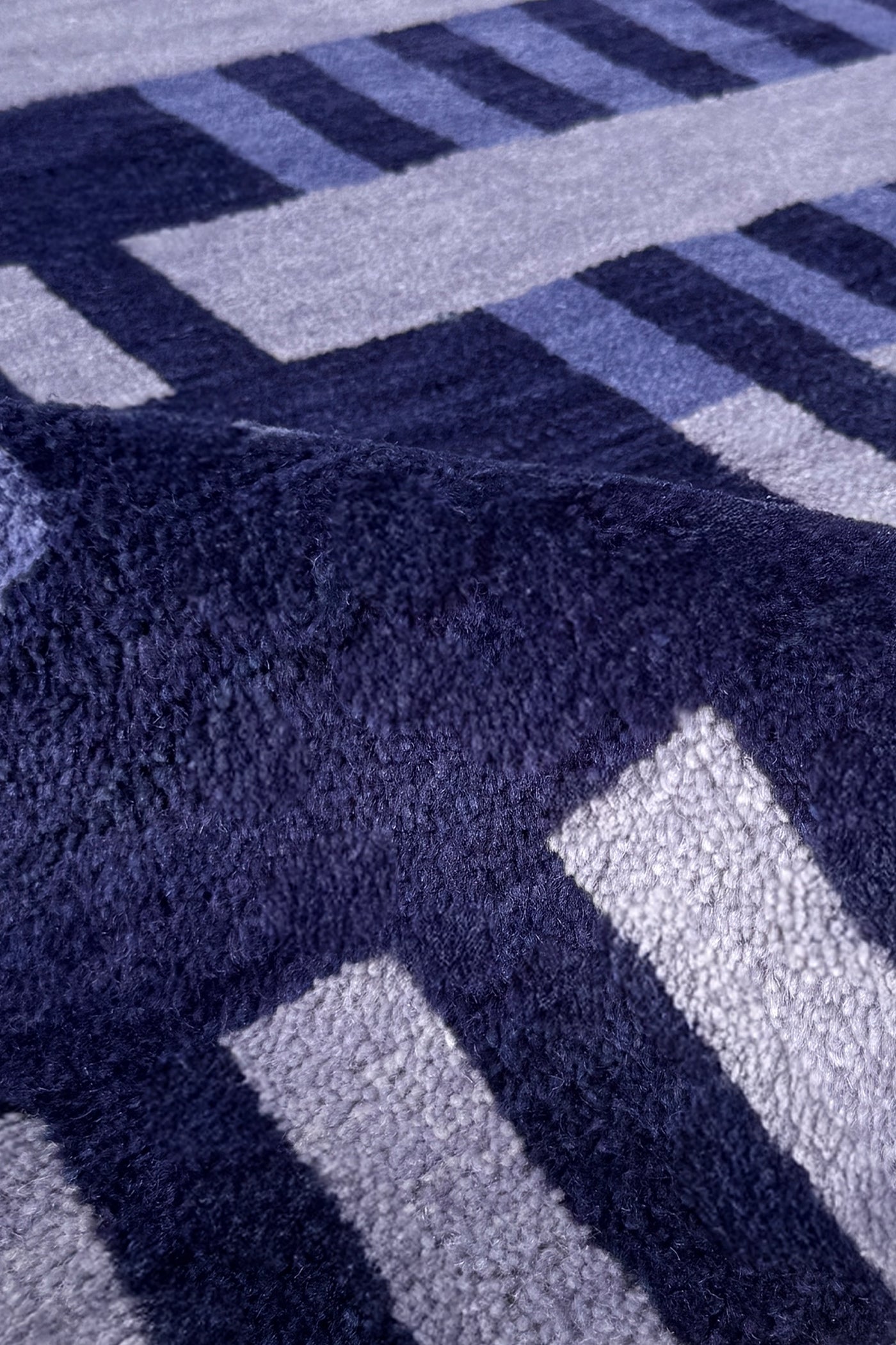 Close-up of a plush textured rug with a geometric pattern in navy blue, light blue, and white.