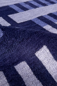 Close-up of a plush textured rug with a geometric pattern in navy blue, light blue, and white.