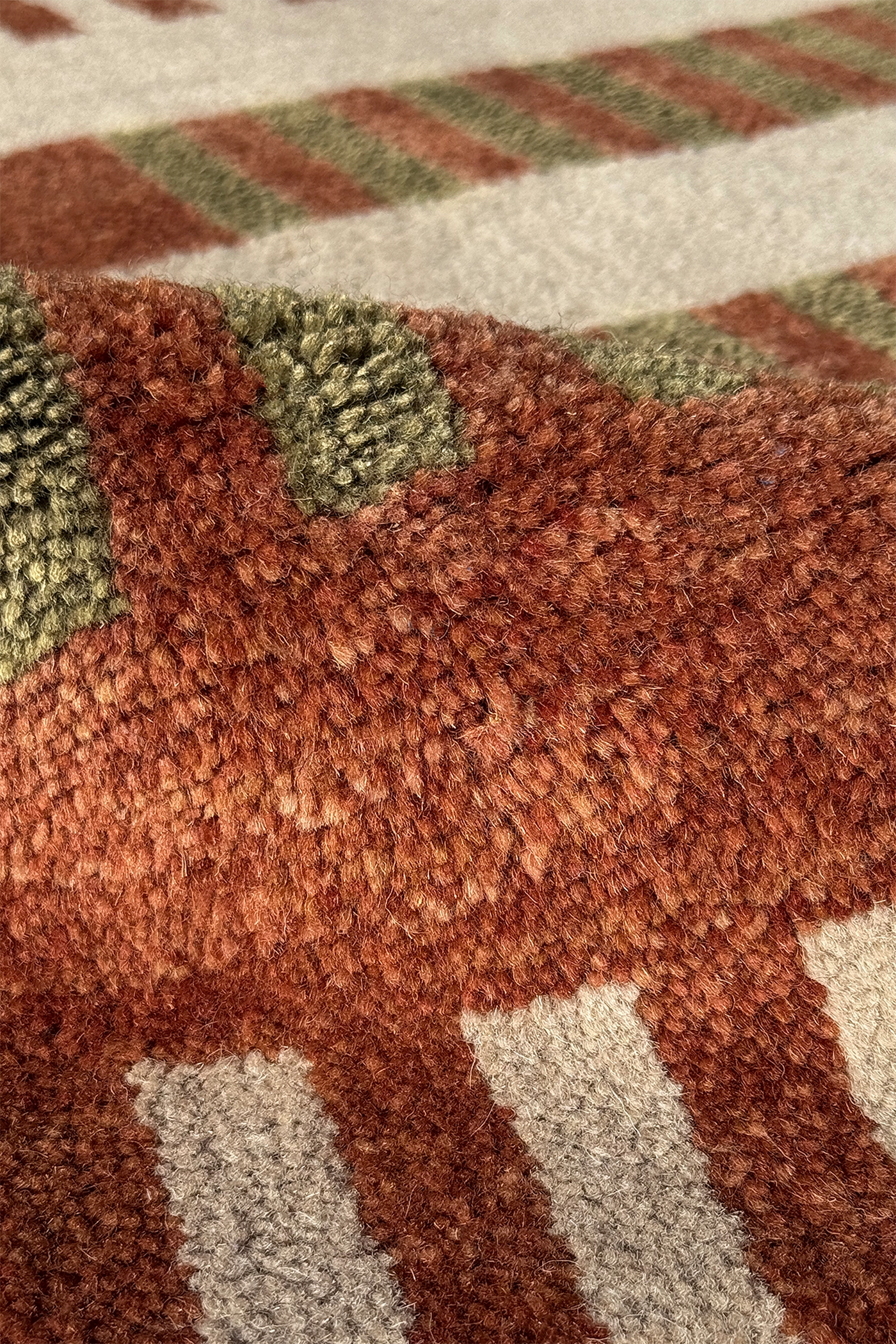 Close-up of a textured corner rug with a geometric pattern in rust brown, sage, and cream multicolor