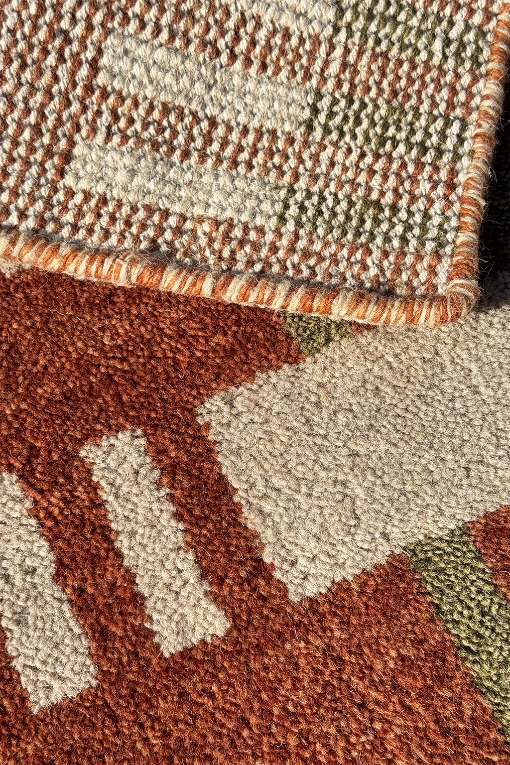 Close-up of a textured area rug with a geometric pattern in rust brown, cream, and olive multicolor, showing the pile texture and corner detail.