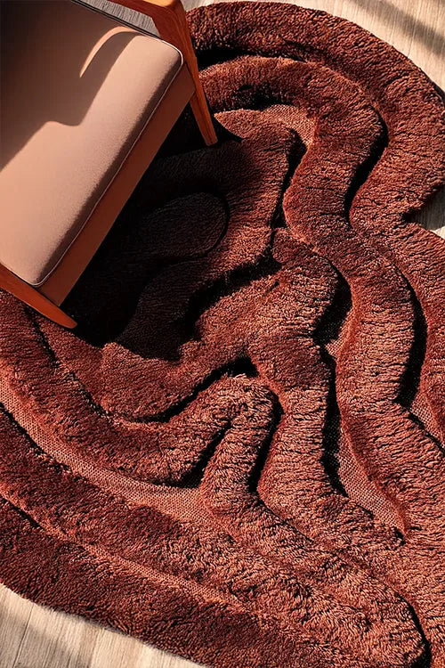 Brown textured shag rug on a wooden floor with a chair partially visible.