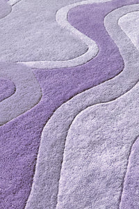 A close-up of a textured area rug with a wavy, layered pattern in shades of lavender purple and light gray.