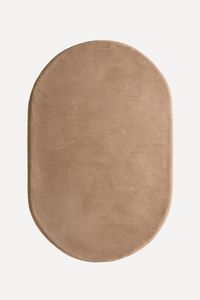 An oval-shaped rug in a warm taupe beige color, shown from a top-down view on a clean white background light brown