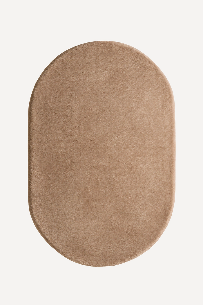 An oval-shaped rug in a warm taupe beige color, shown from a top-down view on a clean white background light brown