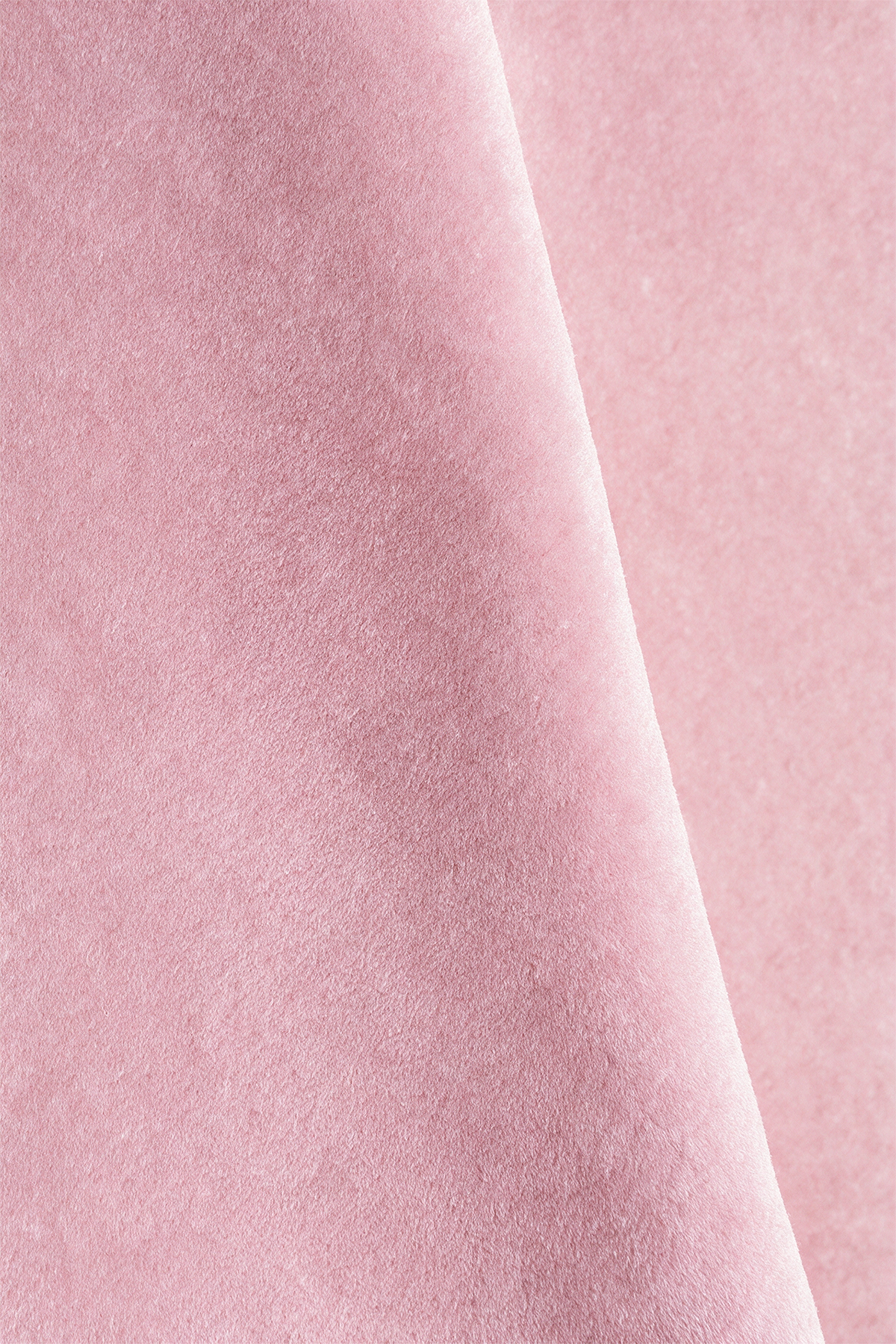 A close-up of soft light pink wool rug with a smooth, slightly velvety texture and a diagonal fold running through the center.