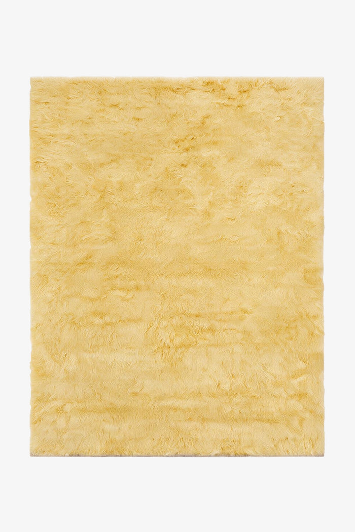 A rectangular pale yellow shaggy wool rug shown from a top-down view on a white background.