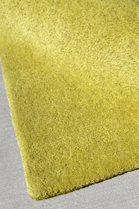 Close-up of the corner of a lime green rug on a gray surface