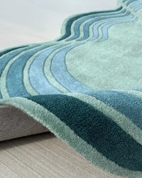 Hourglass-shaped wool rug with teal and aqua waves and curved edges