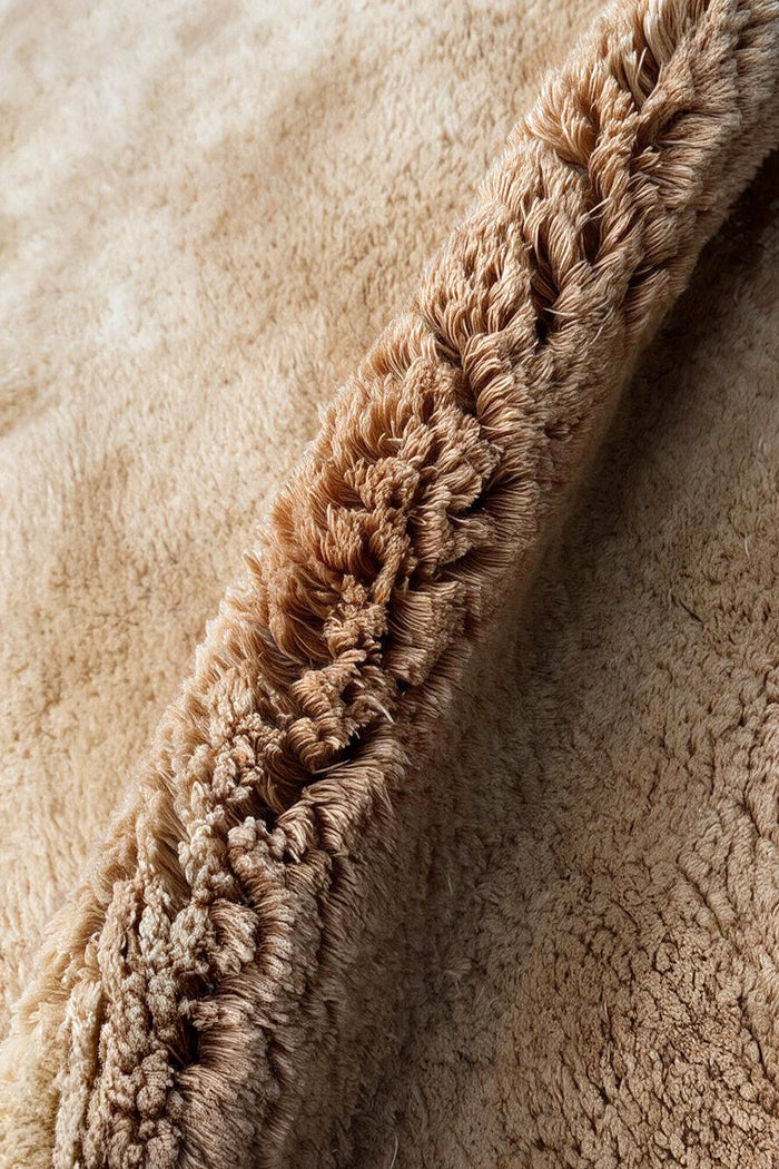 close up texture of a shaggy wool rug with a camel brown color