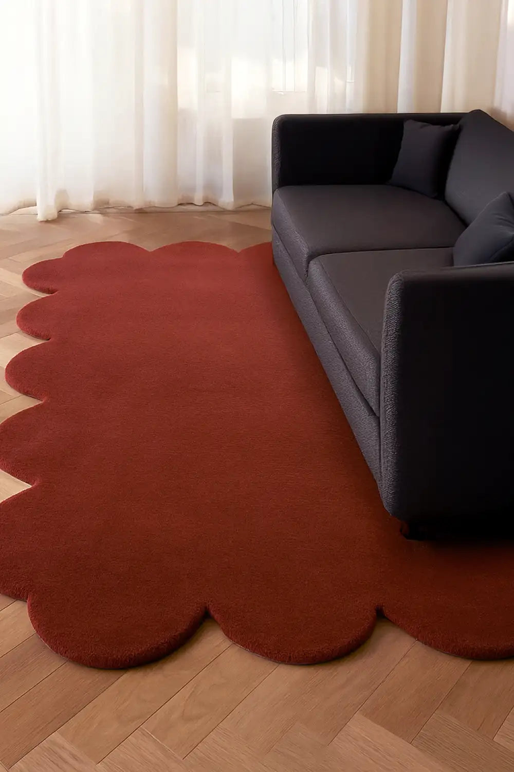 Modern boho rust wool rug with scalloped edges styled under dark sofa on herringbone wood floors