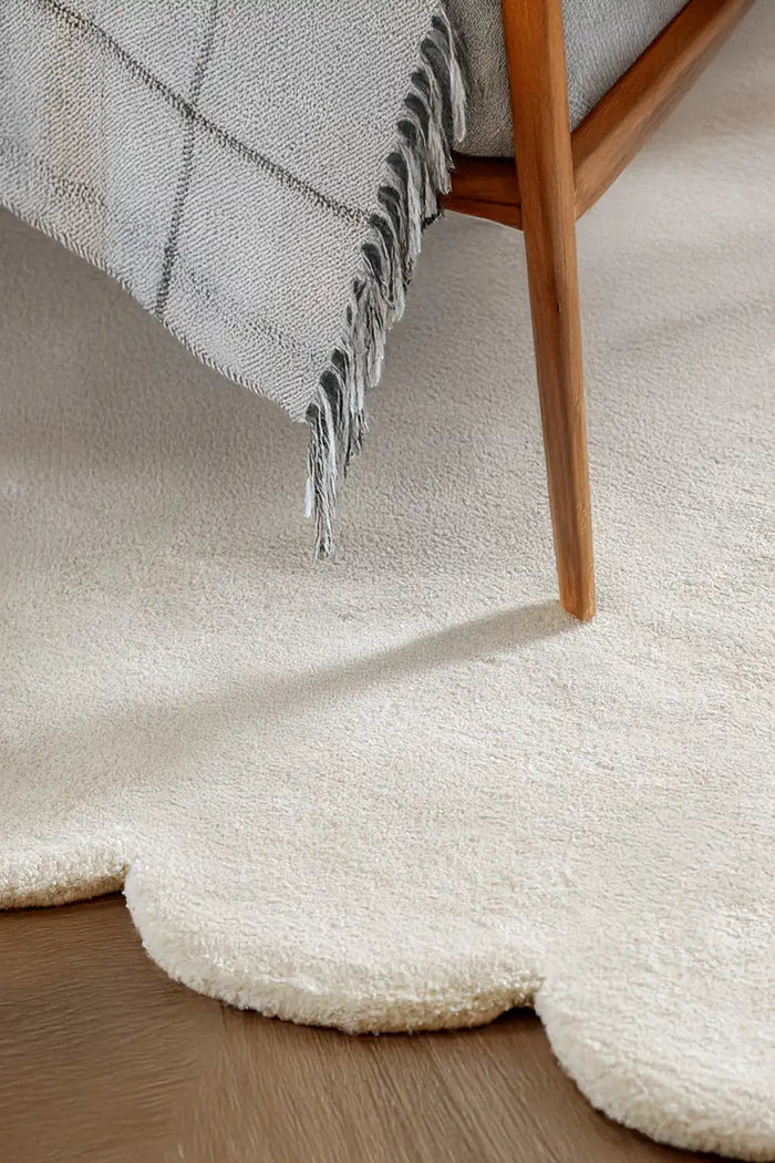 Neutral scalloped edge rug in soft cream wool, shown under wooden accent chair in Japandi-style bedroom