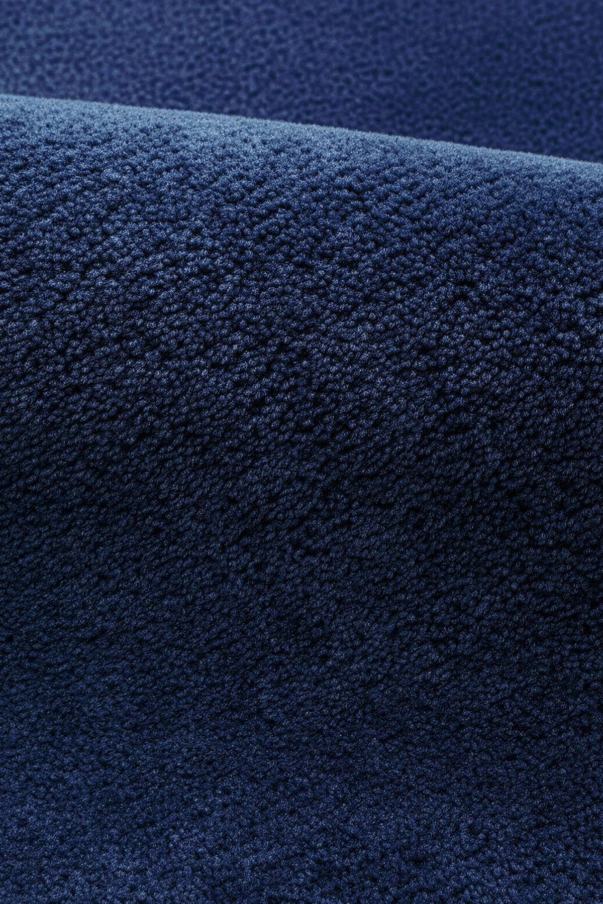 A close-up of a dark navy blue textured rug, showing the detailed wool pile texture and a soft fold.