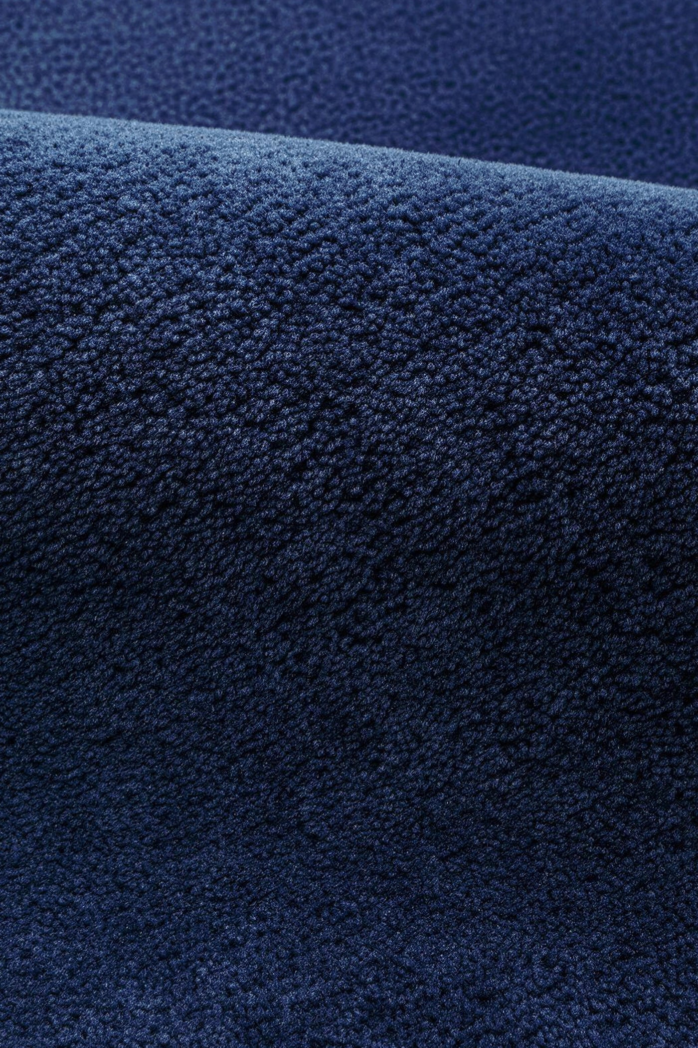 A close-up of a dark navy blue textured rug, showing the detailed wool pile texture and a soft fold.