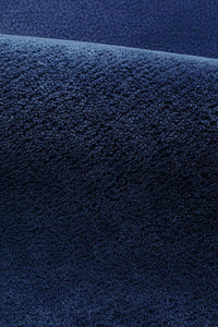 A close-up of a dark navy blue textured rug, showing the detailed wool pile texture and a soft fold.