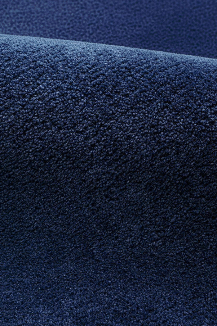 A close-up of a dark navy blue textured rug, showing the detailed wool pile texture and a soft fold.