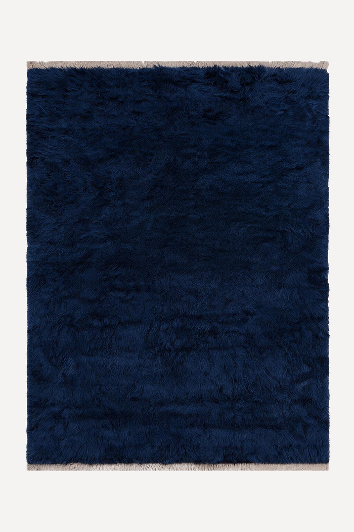 A dark navy blue shaggy area rug with light beige fringe on the top and bottom edges, shown flat against a light off-white background.