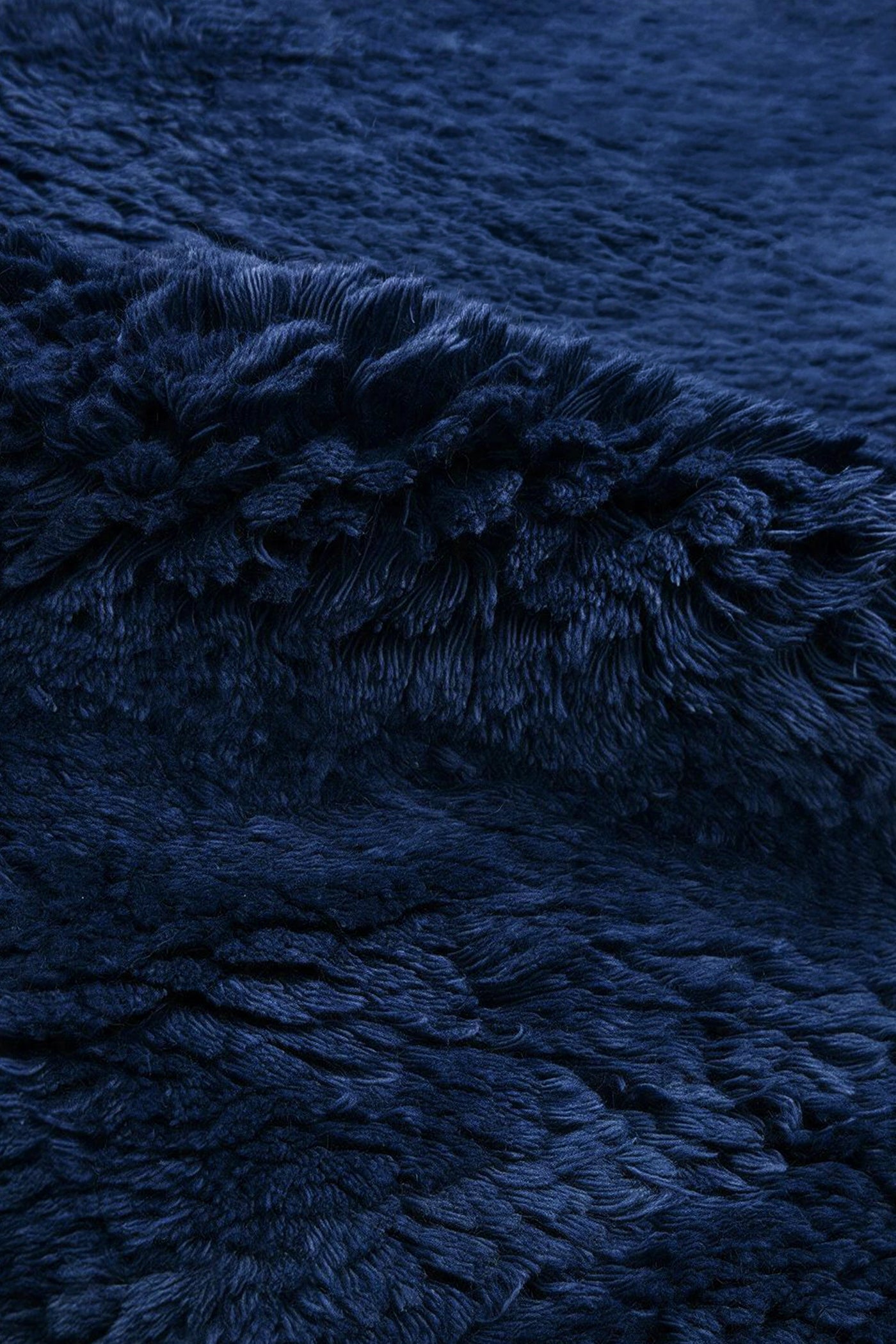 A close-up of a dark navy blue shaggy wool rug, showing the soft, textured pile and draped folds.