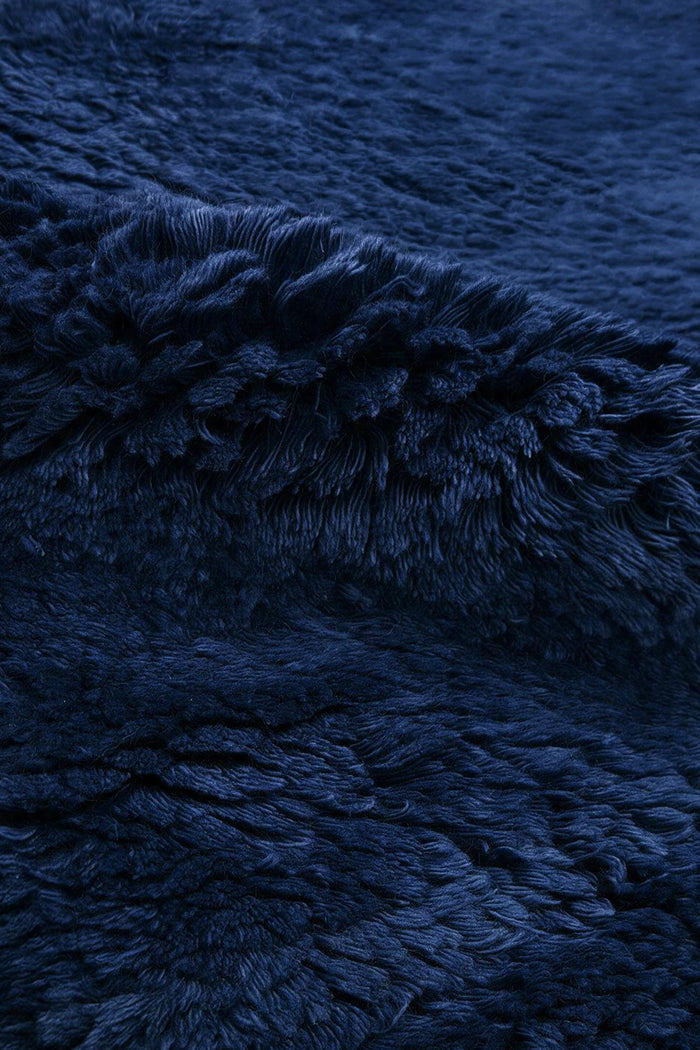A close-up of a dark navy blue shaggy wool rug, showing the soft, textured pile and draped folds.