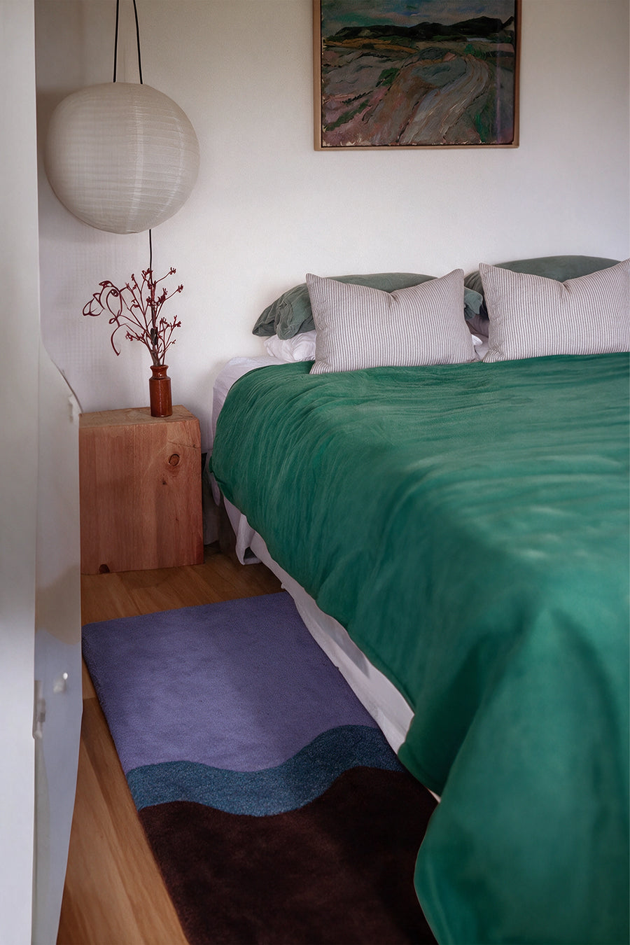 a neapolitan hand-tufted wool runner rug in purple, teal and dark brown waves beside a bed with a green duvet and a wooden nightstand lifestyle