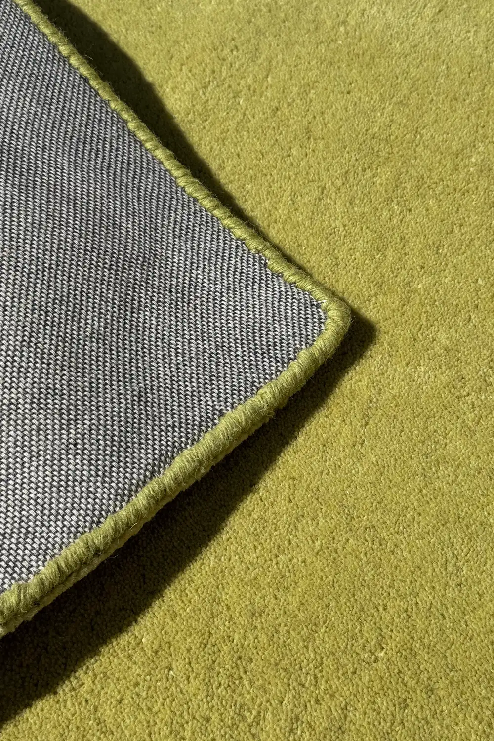 close-up of a neon green wool tufted rug shown with corner flipped to show thick pile and high quality backing