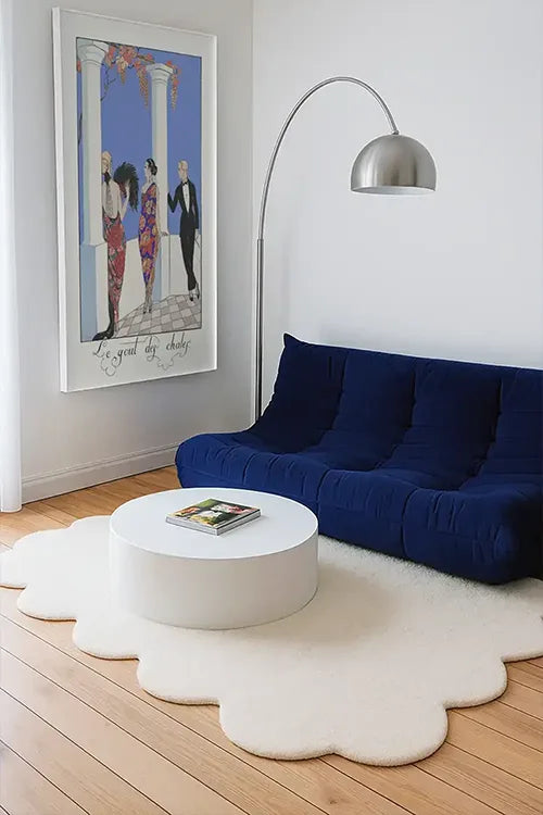 Modern living room with blue sofa, white coffee table, and decorative sculpted white rug.