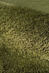 A close-up view of a textured, hand-knotted pile carpet in a muted olive green color, showing the dense wool fibers and slight sheen.