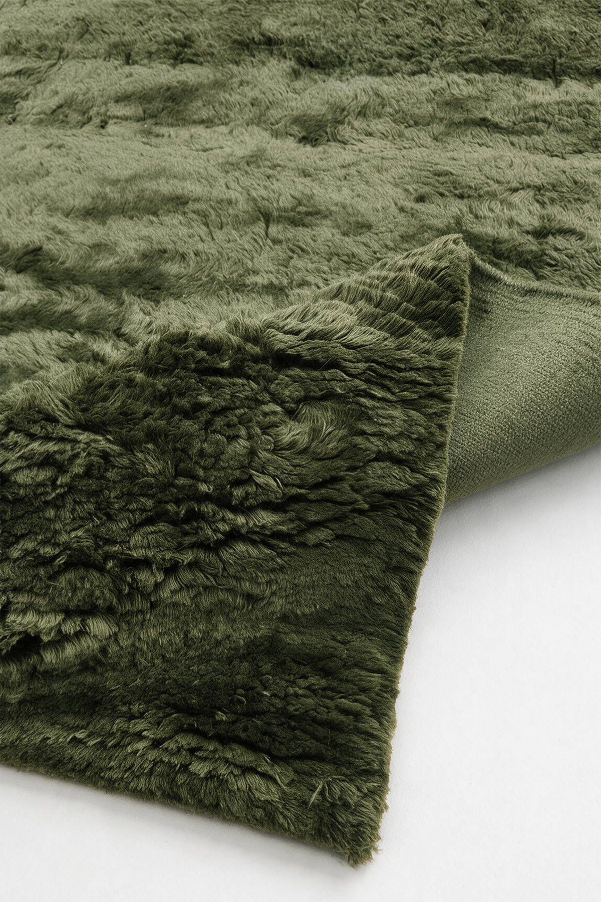 A dark olive green shaggy wool rug with a textured looped pile, folded over to show its soft underside on a clean white background.