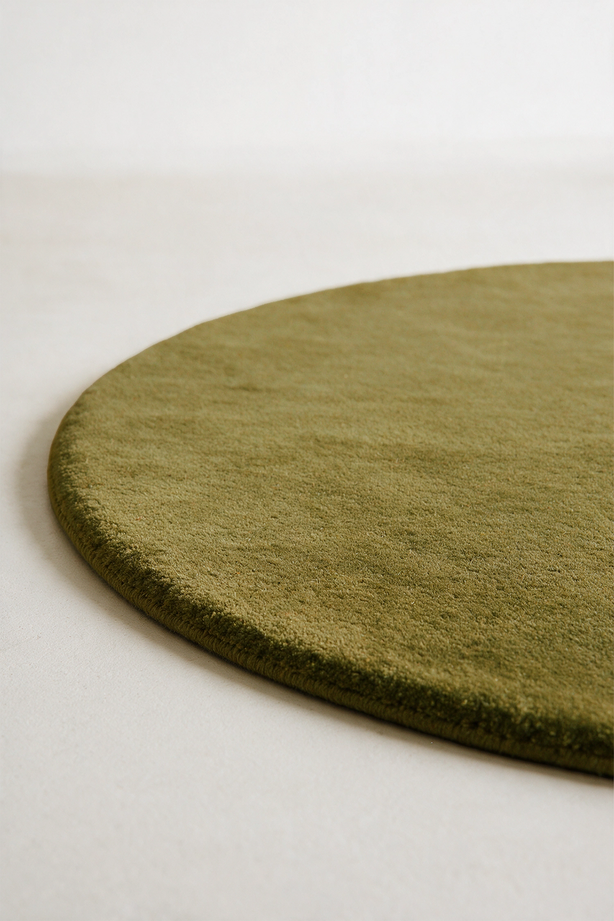 A close-up of a round area rug in olive green, showing its plush texture and curved edge against a neutral off-white background.