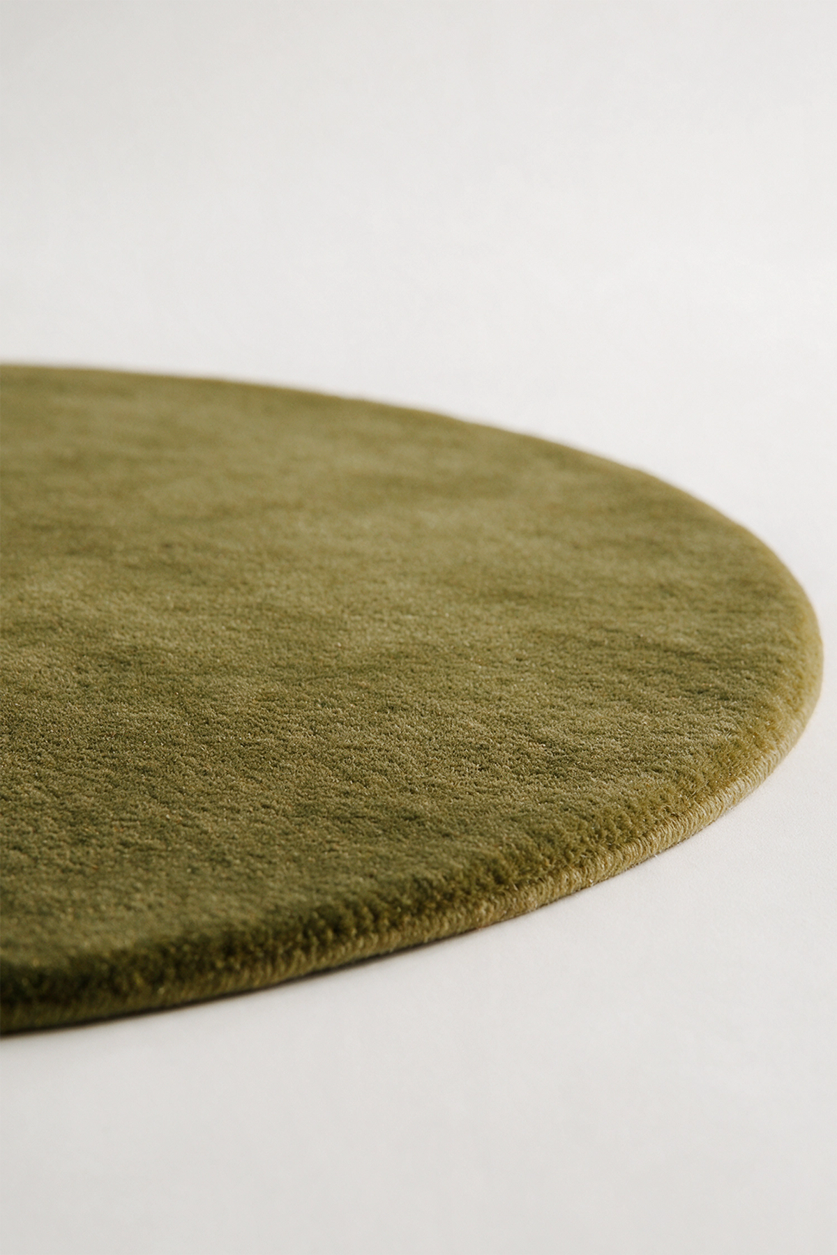 A close-up of a round, olive green textured rug on a clean, light off-white background.