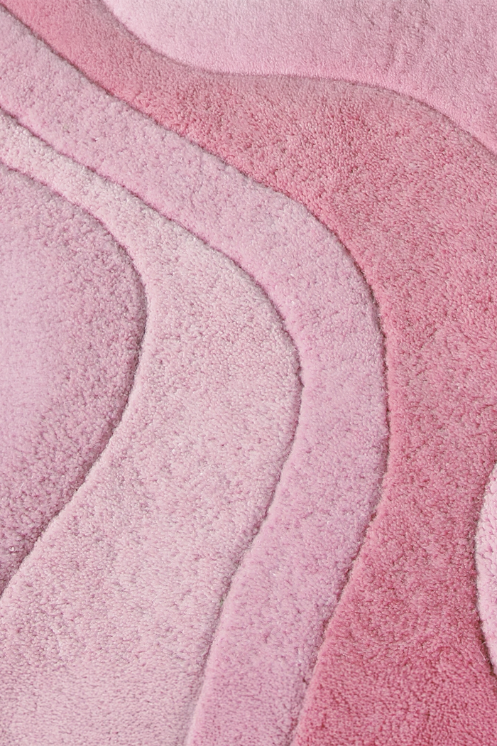 A close-up of a plush, textured pink rose rug with layered, wavy organic patterns in varying shades of light and medium pink.
