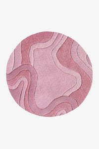 A round area rug featuring an abstract, layered topographic pattern in various shades of dusty pink and mauve, shown against a plain light gray background rose
