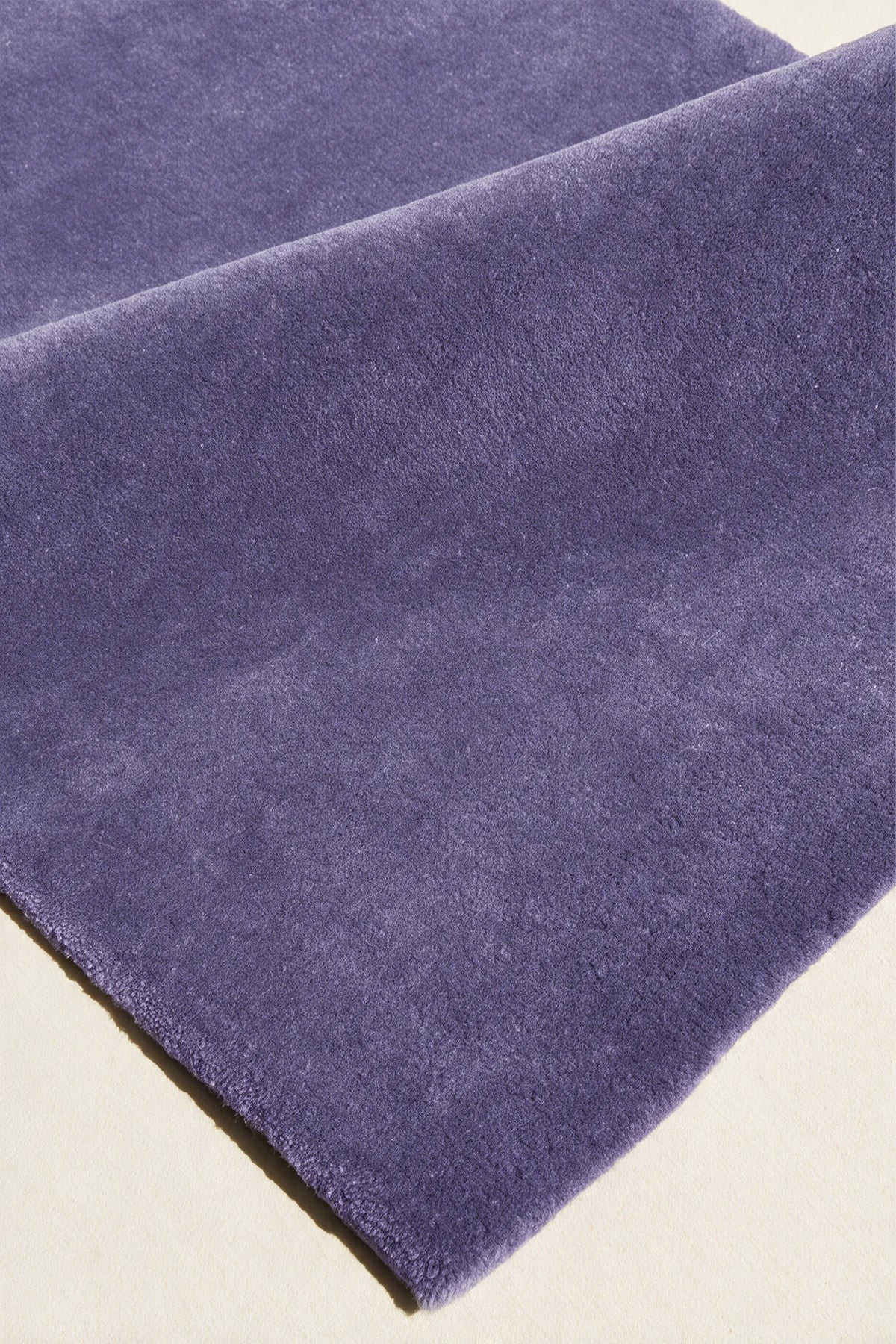 close up texture of a purple cornflower hand-tufted wool rug folded over to show its soft cut pile