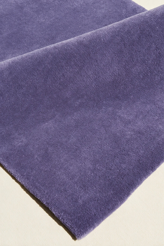 close up texture of a purple cornflower hand-tufted wool rug folded over to show its soft cut pile
