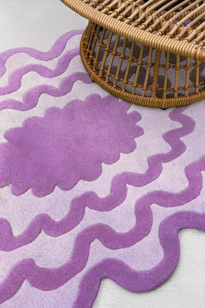 Close-up of purple scalloped wool rug under boho rattan furniture showing wavy oval design lifestyle