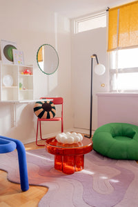 Colorful room with a red chair, lavender purple rug, green bean bag, and orange table.