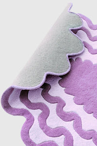 Back side of purple scalloped wool rug showing hand-tufted texture and wavy modern design.